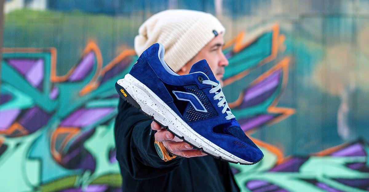 Stylish man presenting blue sneaker against vibrant urban graffiti, showcasing modern fashion.