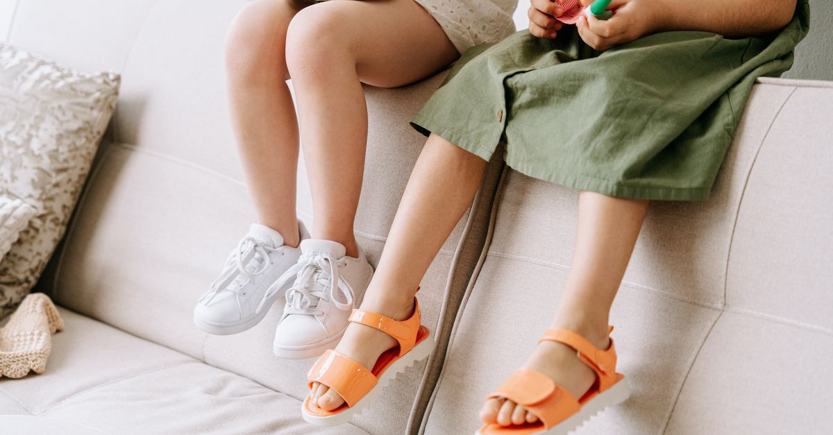 Two children sitting on a couch, showcasing colorful shoes and playful mood.