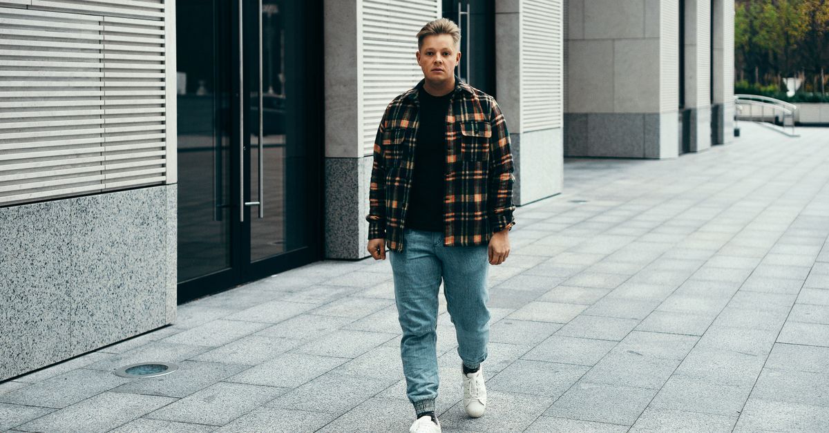 Young man walking on a stone pavement in Minsk, wearing a plaid shirt and jeans.