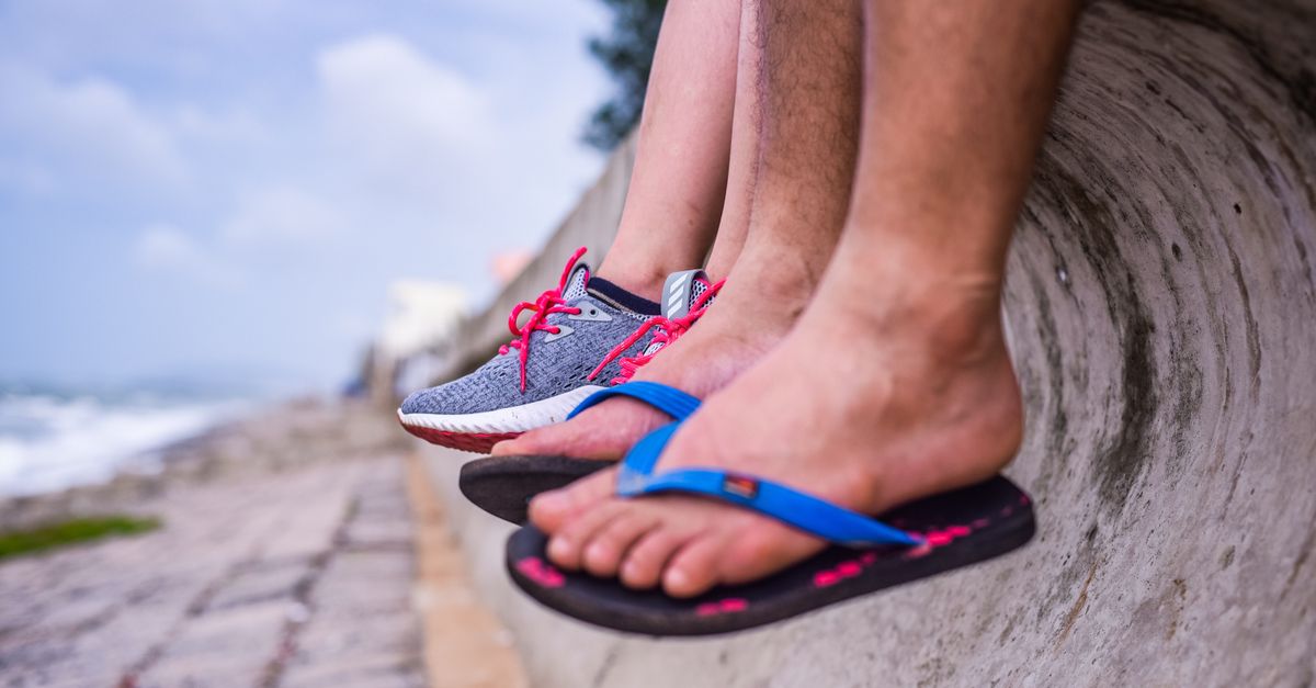 Feet in sneakers and flip-flops resting on a seaside wall with ocean view.