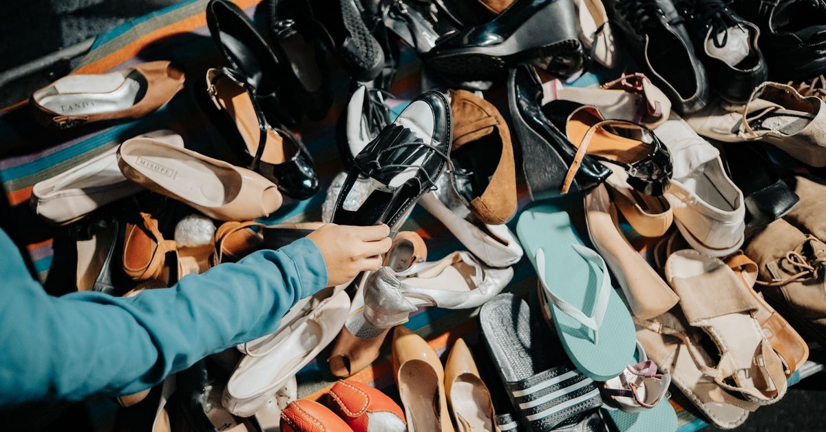 A variety of footwear displayed at an outdoor market stall with a hand selecting a shoe.