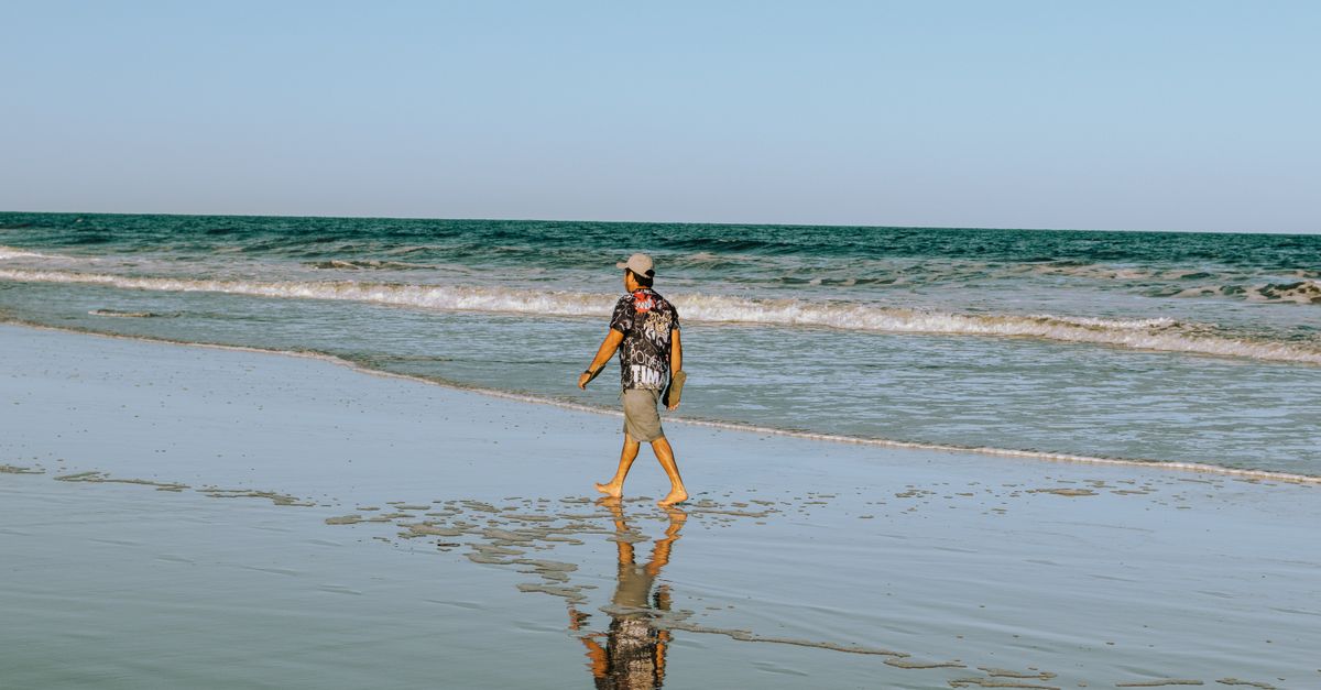 A man walks barefoot on a sunny beach, enjoying a peaceful vacation day by the sea.