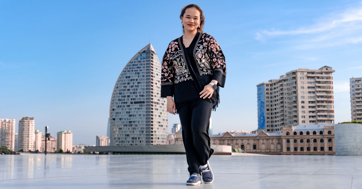 Woman walking in a cityscape with modern architecture and clear blue skies, exuding confidence.