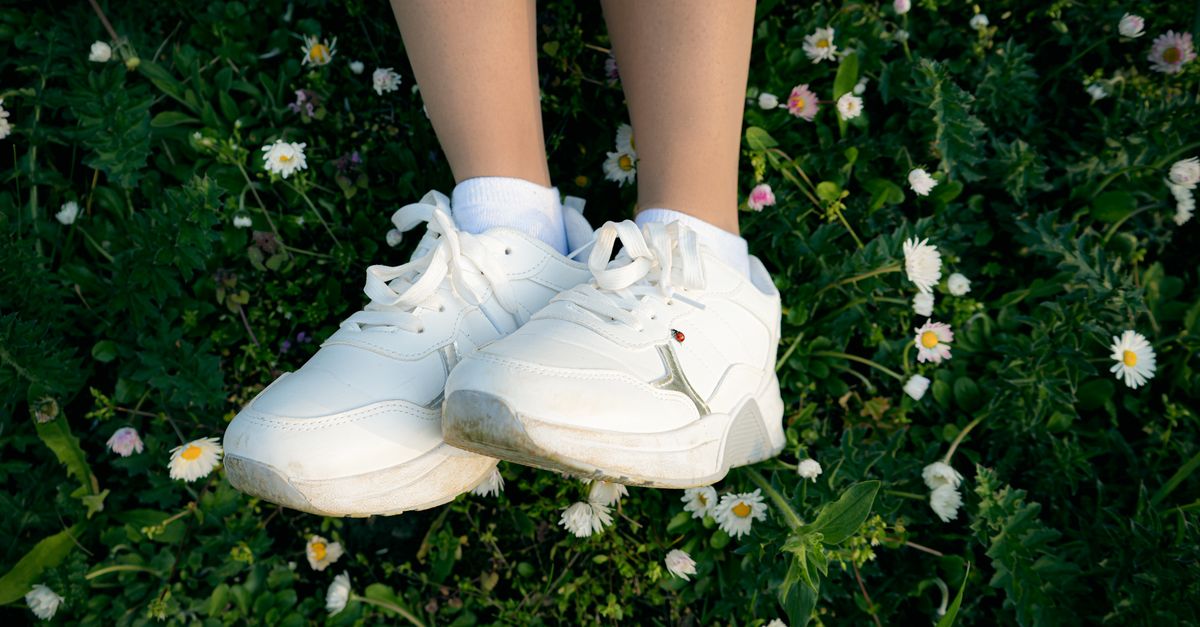 Close-up of white sneakers on grass surrounded by daisies, symbolizing nature and casual lifestyle.