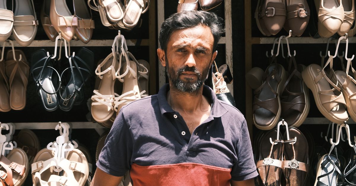 Portrait of a sandal vendor in Bengaluru, showcasing footwear collection in an outdoor market.