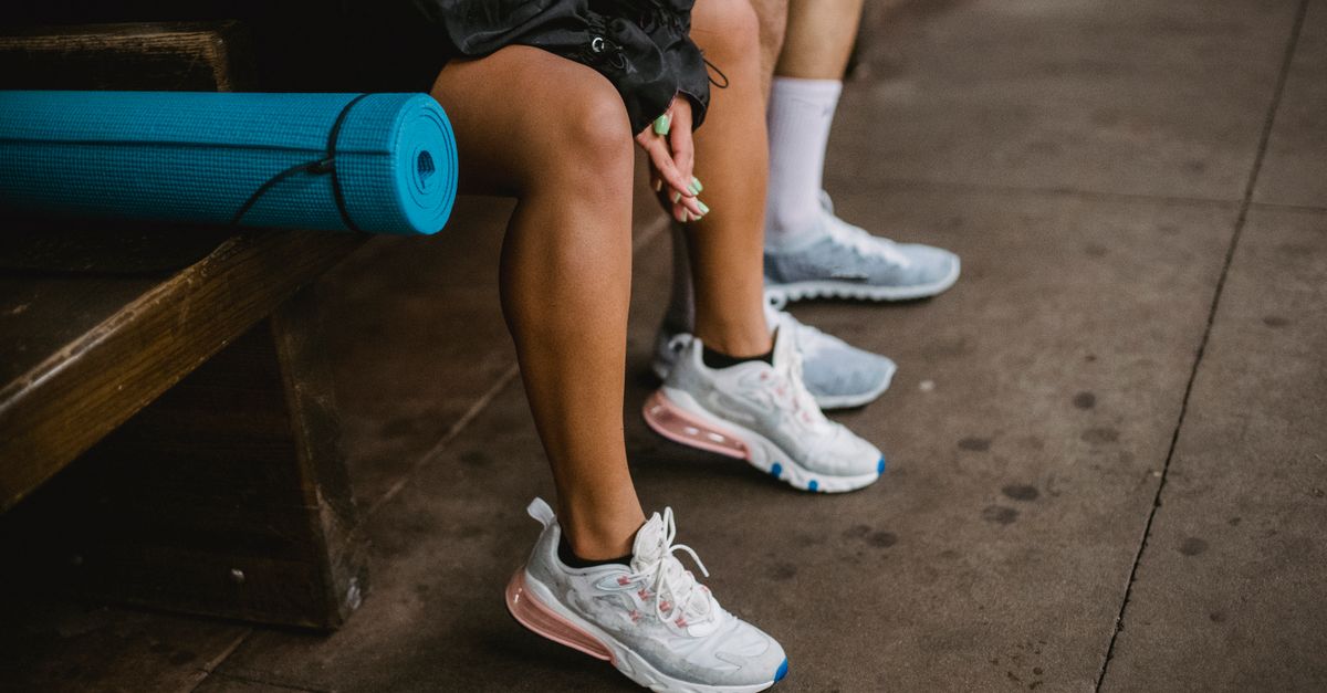 Close-up of two people sitting on a bench with a blue yoga mat and stylish sneakers.