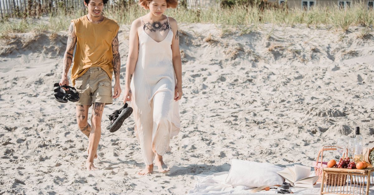 Asian couple walking on a sandy beach after a romantic picnic under the sun.