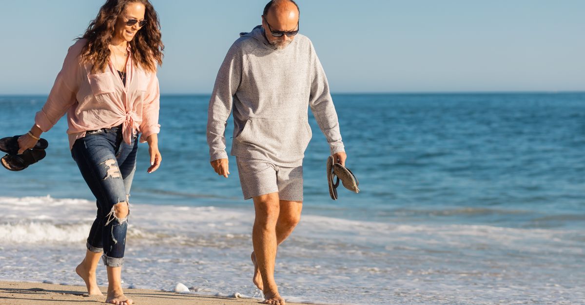 A senior couple enjoying a walk on the sandy beach in the warm summer sun.