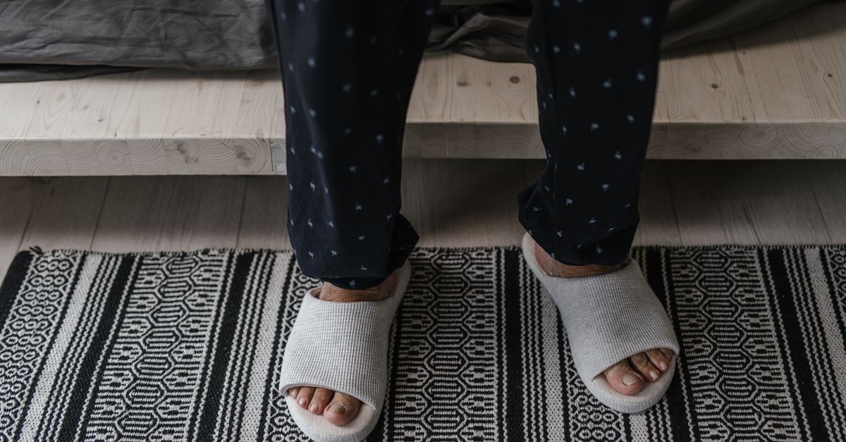 A person stands in soft slippers and polka dot pajamas on a patterned rug.