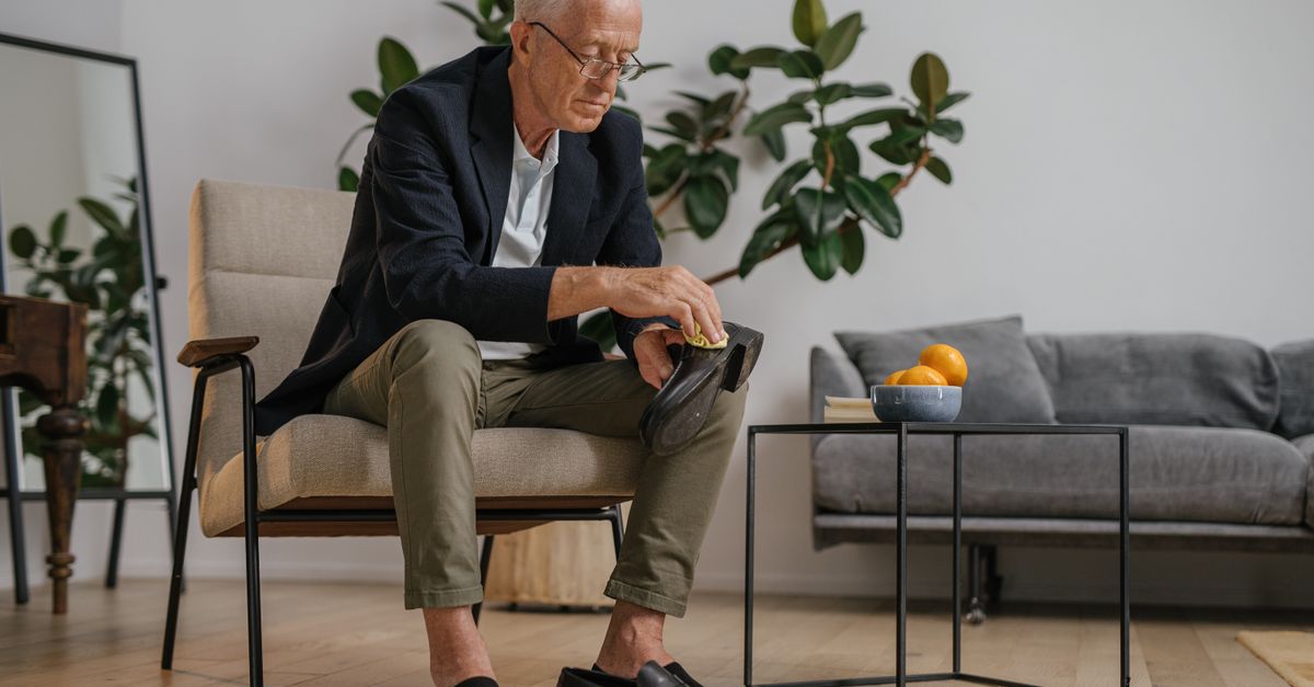 Elderly man polishing shoes at home. Lifestyle and daily grooming indoors.