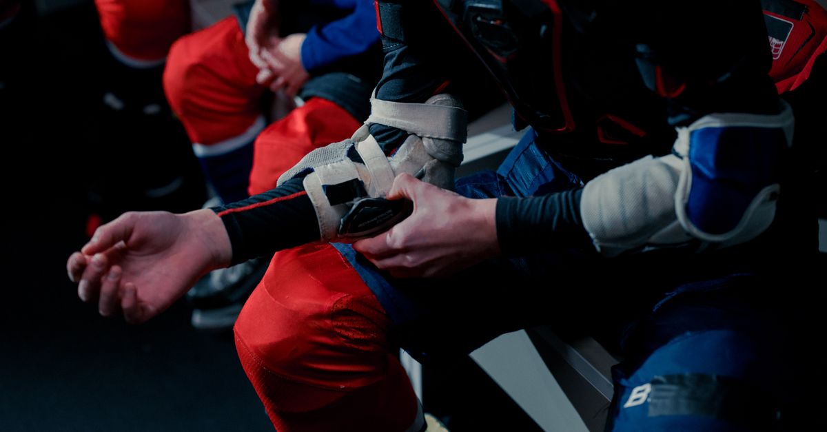 Teen hockey players getting ready in a locker room, adjusting safety gear and shoulder pads.